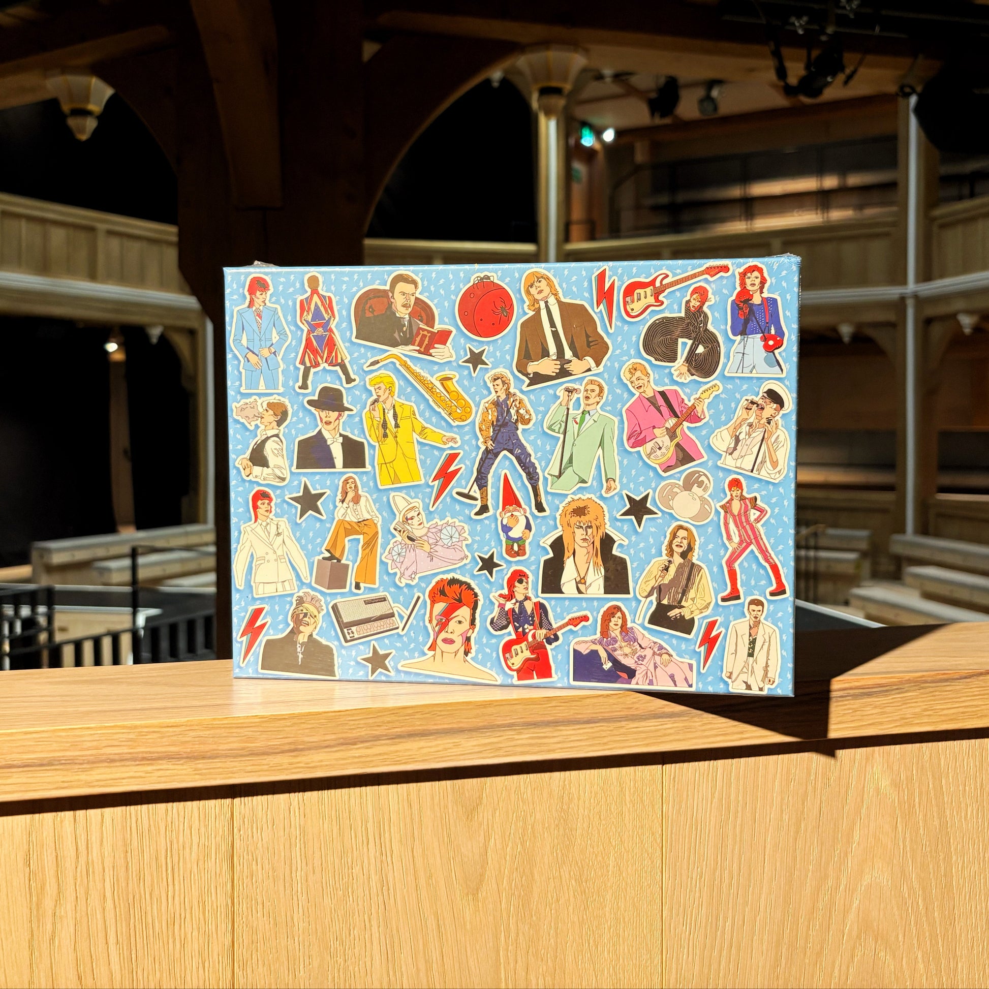 The front of a box for the David Bowie jigsaw puzzle. It is a light blue box featuring lots of pictures of David Bowie.