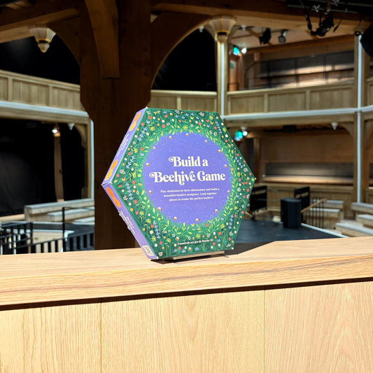 Hexagonal game box titled 'Build a Bechive Game' on a wooden platform with theater seats in the background