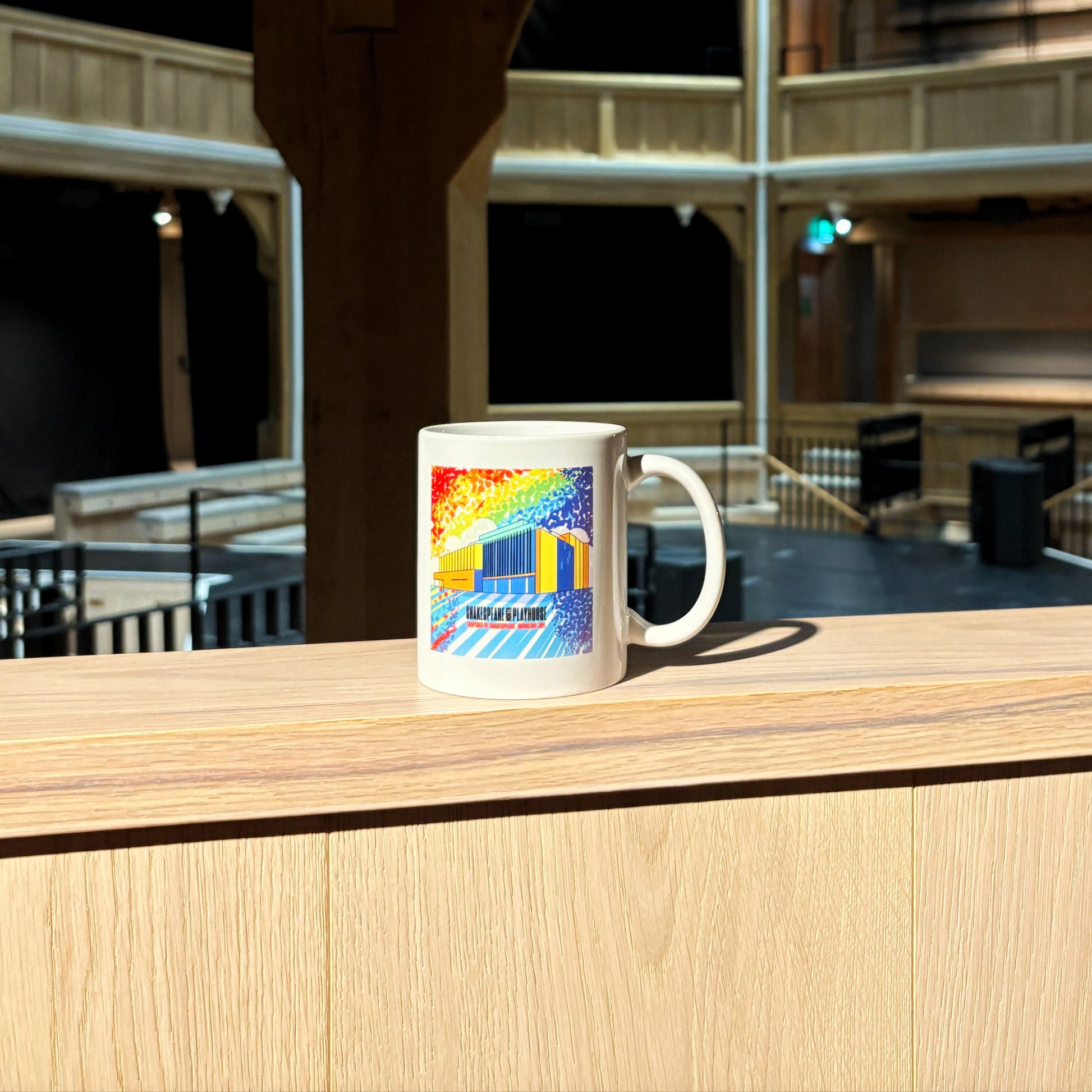 White mug featuring a rainbow illustration of the Shakespeare North building